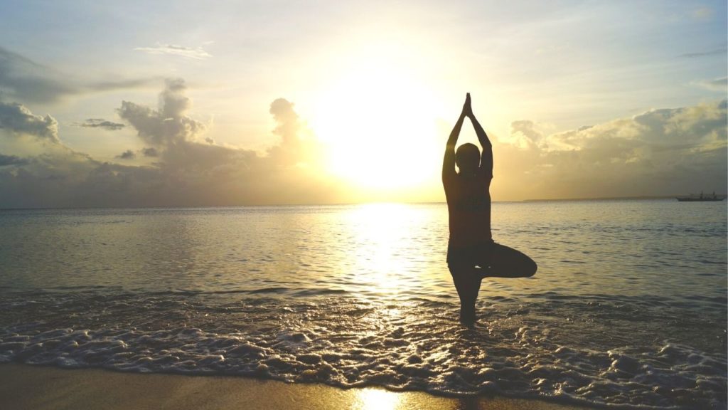 Woman doing yoga on the beach at sunrise