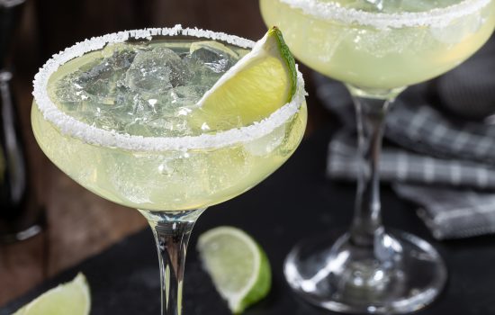 Margarita cocktail with ice, lime and salt rim on a black slate board