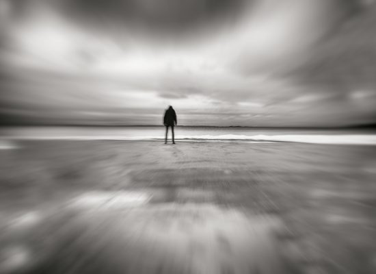 Silhouette of person standing head down on deserted beach in wintertime, motion blur.
