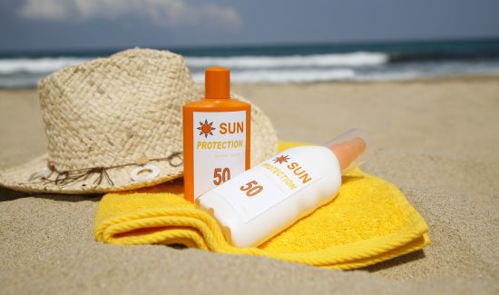 "Sun tan lotion on a sandy beach with a sun hat and yellow towel, waves in the background.N.B. Sun tan lotion labels are factitious and made by ourselves."